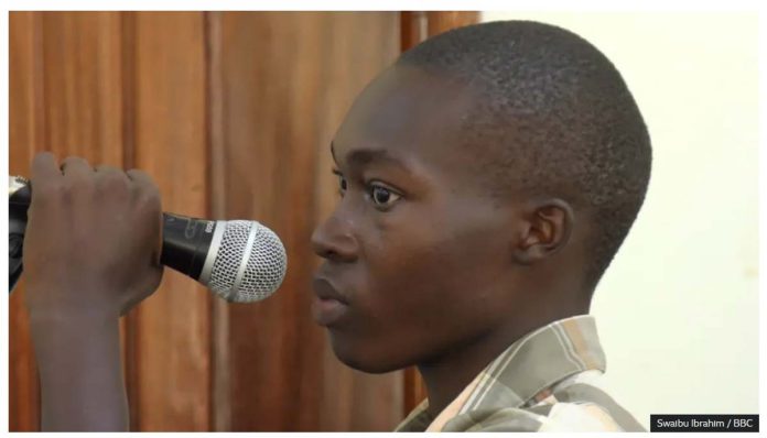 Emmanuel Nabugodi, Ugandan TikToker who has been jailed, holds a microphone in court. He created a mock trial of President Yoweri Museveni. SWAIBU IBRAHIM / BBC