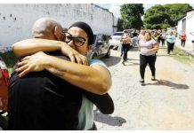 Two people are seen embracing tightly on a street in Tocuyito, Venezuela, with a group of people walking in the background and cars parked along the road. Venezuela released over 100 people arrested following July’s contested presidential election. REUTERS