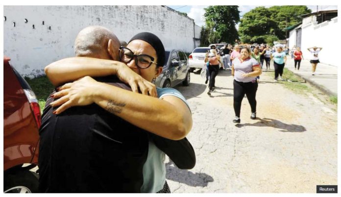 Two people are seen embracing tightly on a street in Tocuyito, Venezuela, with a group of people walking in the background and cars parked along the road. Venezuela released over 100 people arrested following July’s contested presidential election. REUTERS