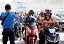 A motorcycle rider flashes the thumbs-up sign to a traffic constable carrying a placard that reads “Motorcycle Lane Exclusive for Motorcycle” along Commonwealth Avenue in Quezon City. PNA