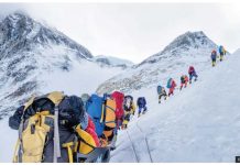 A line of mountain climbers hike across a snow-covered slope with mountain peaks in the background. Nepal is often criticized for allowing too many climbers on Everest. GETTY IMAGES