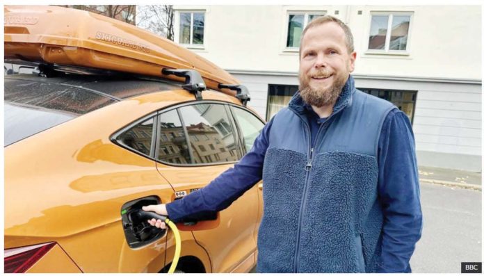 Norwegian motorist Ståle Fyen smiles as he attaches a charging cable to his electric car. Like a third of Norwegian motorists, Fyen now drives an electric car. BBC