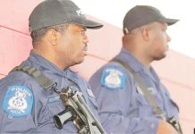 Two armed policemen in Port of Spain, Trinidad, seen in profile wearing black baseball caps and blue shirts. GETTY IMAGES