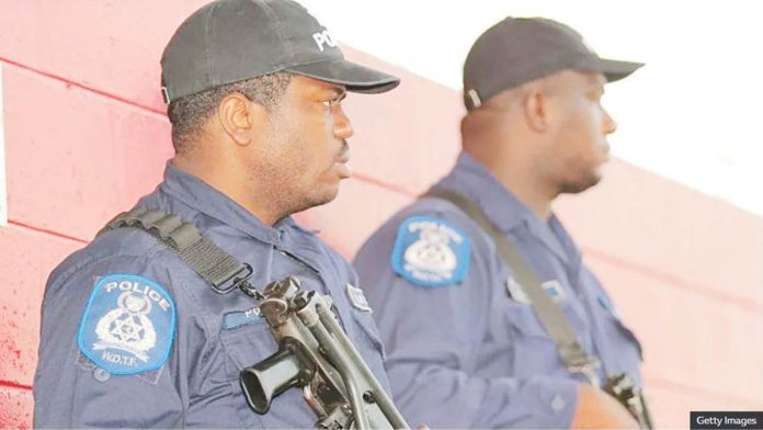 Two armed policemen in Port of Spain, Trinidad, seen in profile wearing black baseball caps and blue shirts. GETTY IMAGES