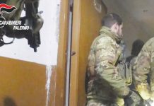 Two uniformed officers of the Carabinieri wearing jackets with a camouflage print stand in a doorway while a colleague behind them holds a gun. Italy's military police launched the operation in the early hours of Tuesday against the Mafia. CARABINIERI PALERMO