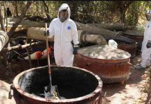 Two Mexican army personnel wearing white protective suits, full face visors and heavy-duty black gloves stand in front of large vats at a site which was used as a meth laboratory in the community of Higueras de Abuya in Mexico. REUTERS