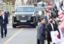 South Korean impeached President Yoon Suk Yeol walks outside the Seoul detention center after his release, in Uiwang, with crowds of supporters waving South Korea flags and a police convoy behind him. REUTERS