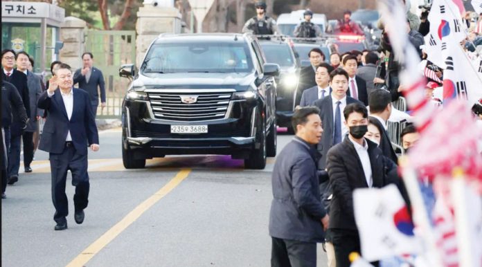 South Korean impeached President Yoon Suk Yeol walks outside the Seoul detention center after his release, in Uiwang, with crowds of supporters waving South Korea flags and a police convoy behind him. REUTERS