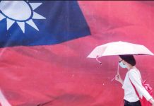 A woman carrying an umbrella walks past a giant Taiwan flag. GETTY IMAGES