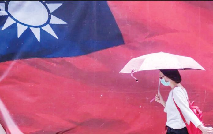 A woman carrying an umbrella walks past a giant Taiwan flag. GETTY IMAGES