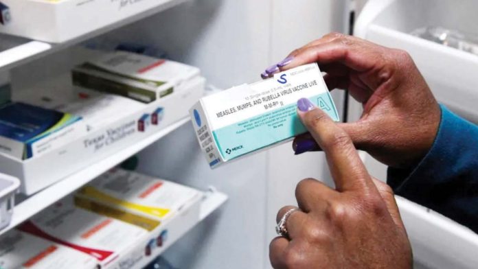 A box containing the vaccine against measles, mumps and rubella, is being held by a woman with her right hand. REUTERS