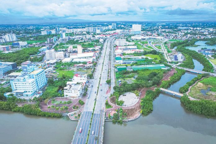 A bird’s-eye view of Iloilo City’s Mandurriao district, especially the New Business District, reveals a landscape transformed by rapid urban development. The district has become a vibrant hub of activity with high-rise buildings housing business process outsourcing (BPO) and other office spaces, modern residential complexes, and bustling commercial spaces. The photo also illustrates that despite the modernization, Iloilo City strikes a balance with green initiatives. This is evident in the clean Iloilo River, thriving mangroves, and well-maintained green open spaces.